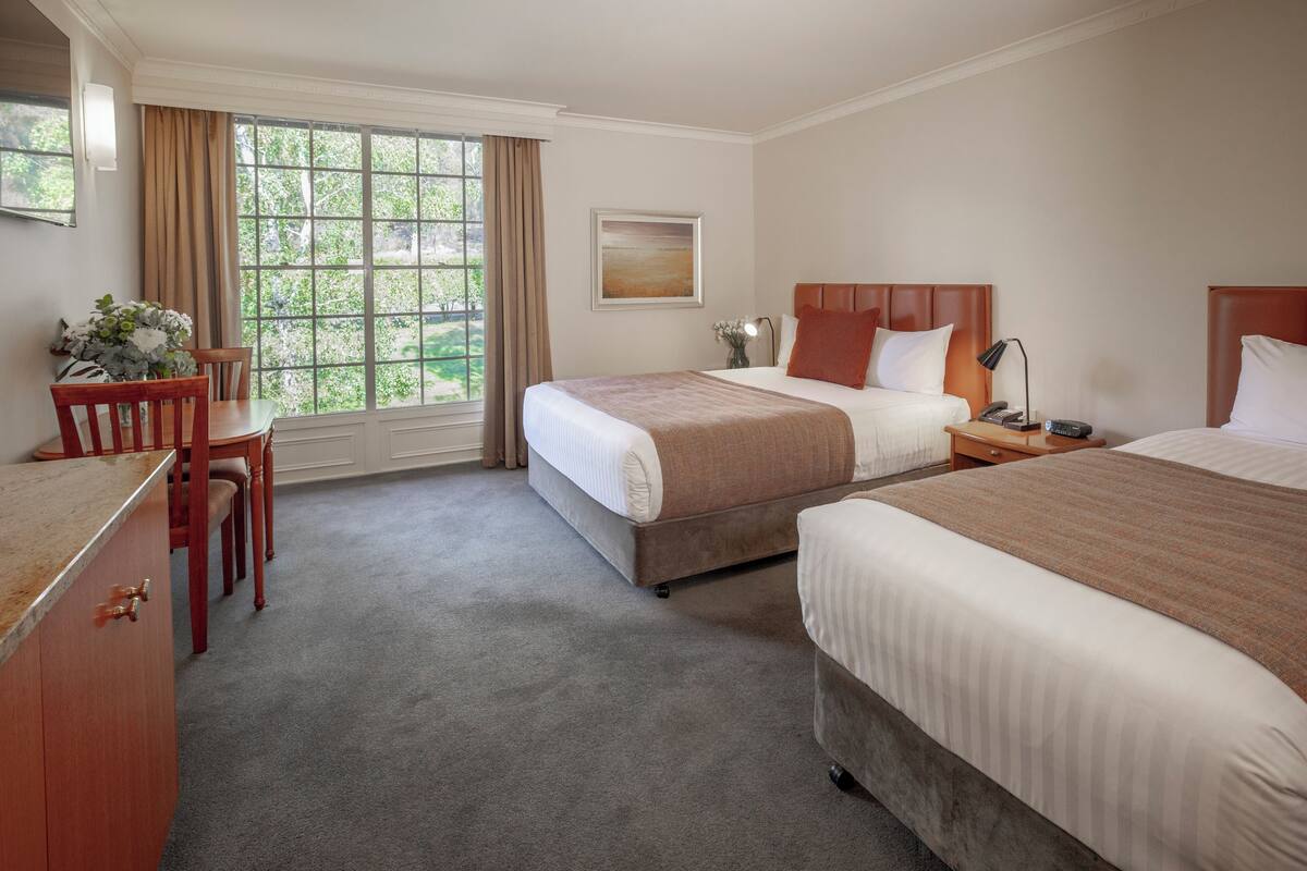 A hotel room with two beds, a desk, and a window with curtains.