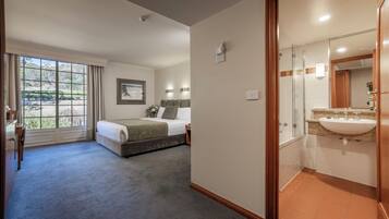 A hotel room with a large window, a bed, a bedside table, a mirror, and a bathroom with a sink and toilet.