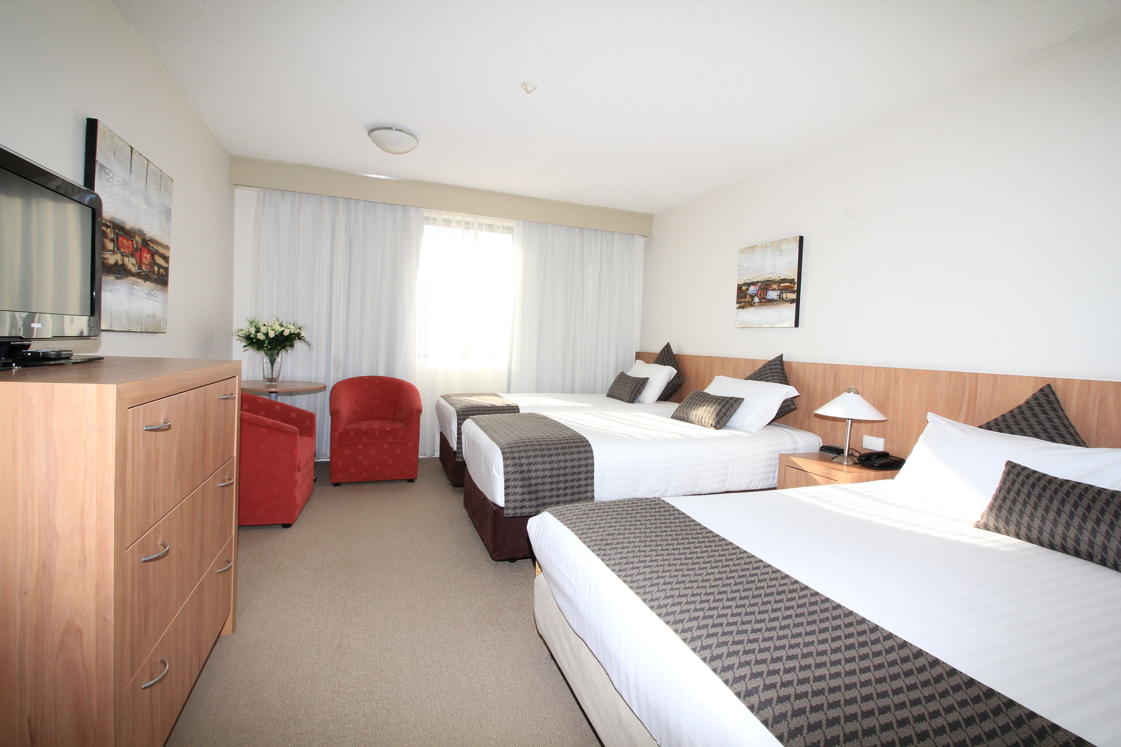 A hotel room with two beds, a desk, a TV, and a red chair.