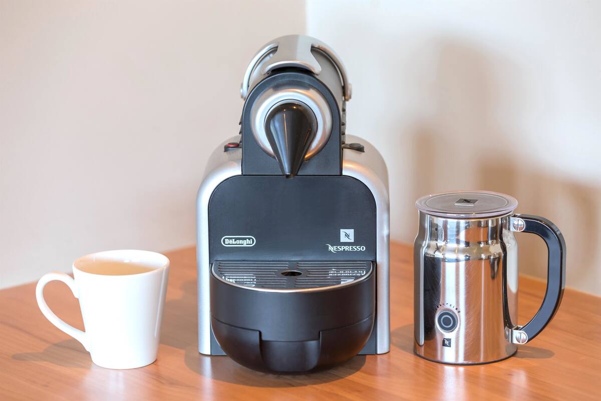 A coffee machine, a white mug, and a stainless steel coffee pot on a wooden table.