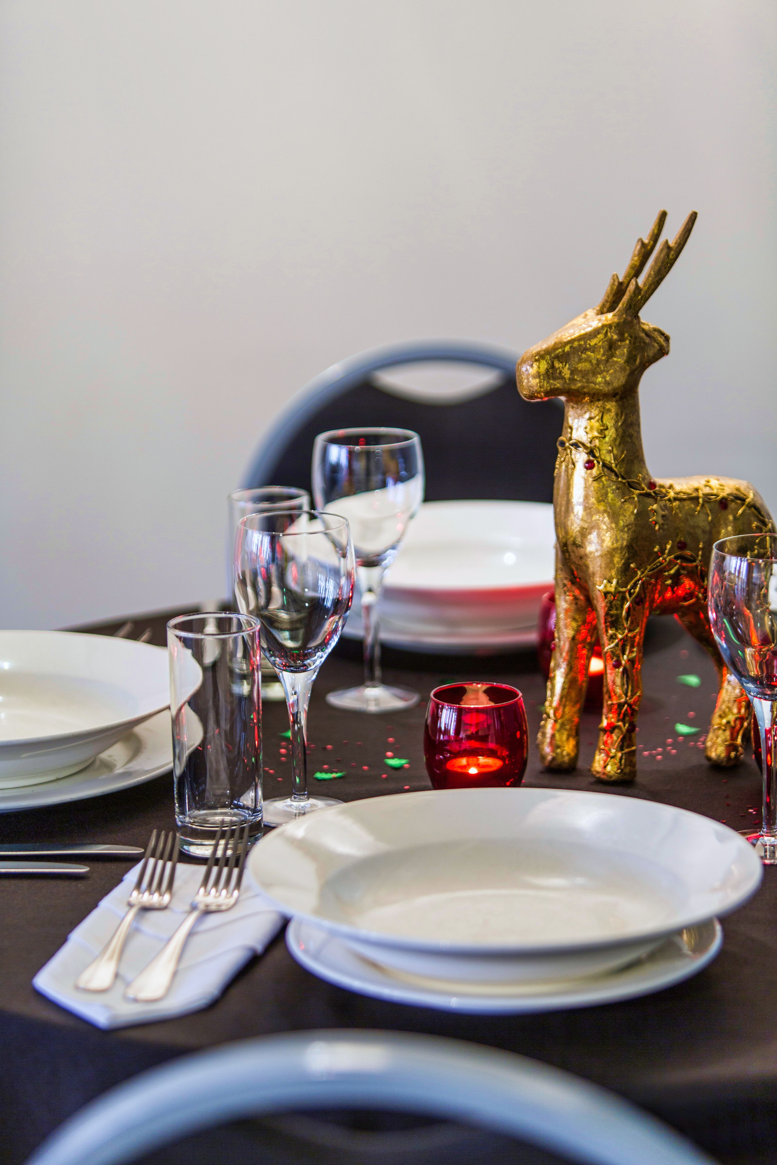 A dining table set with plates, glasses, and cutlery, and a decorative golden reindeer figurine.