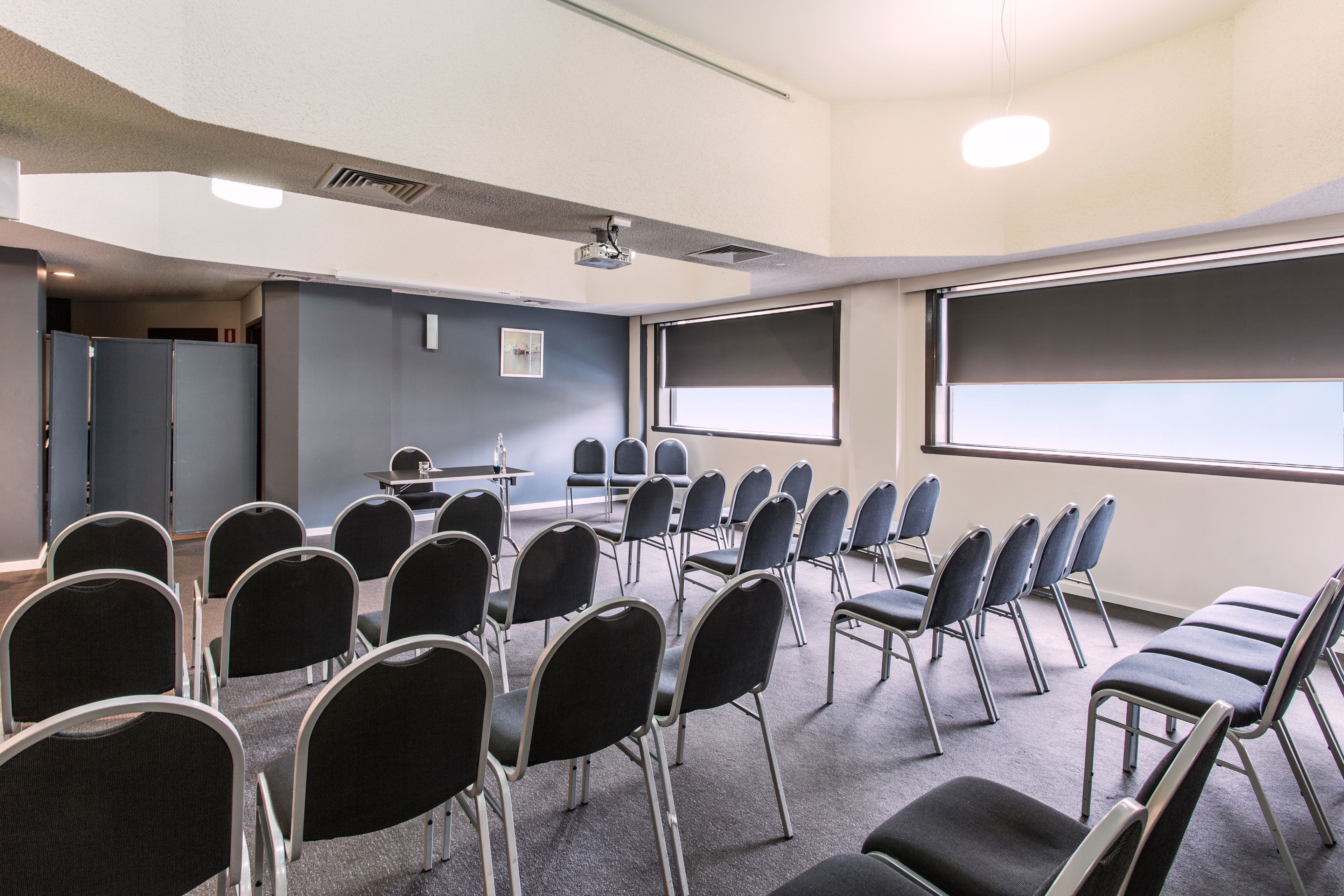 A conference room with rows of chairs, a projector screen, and a presentation area.