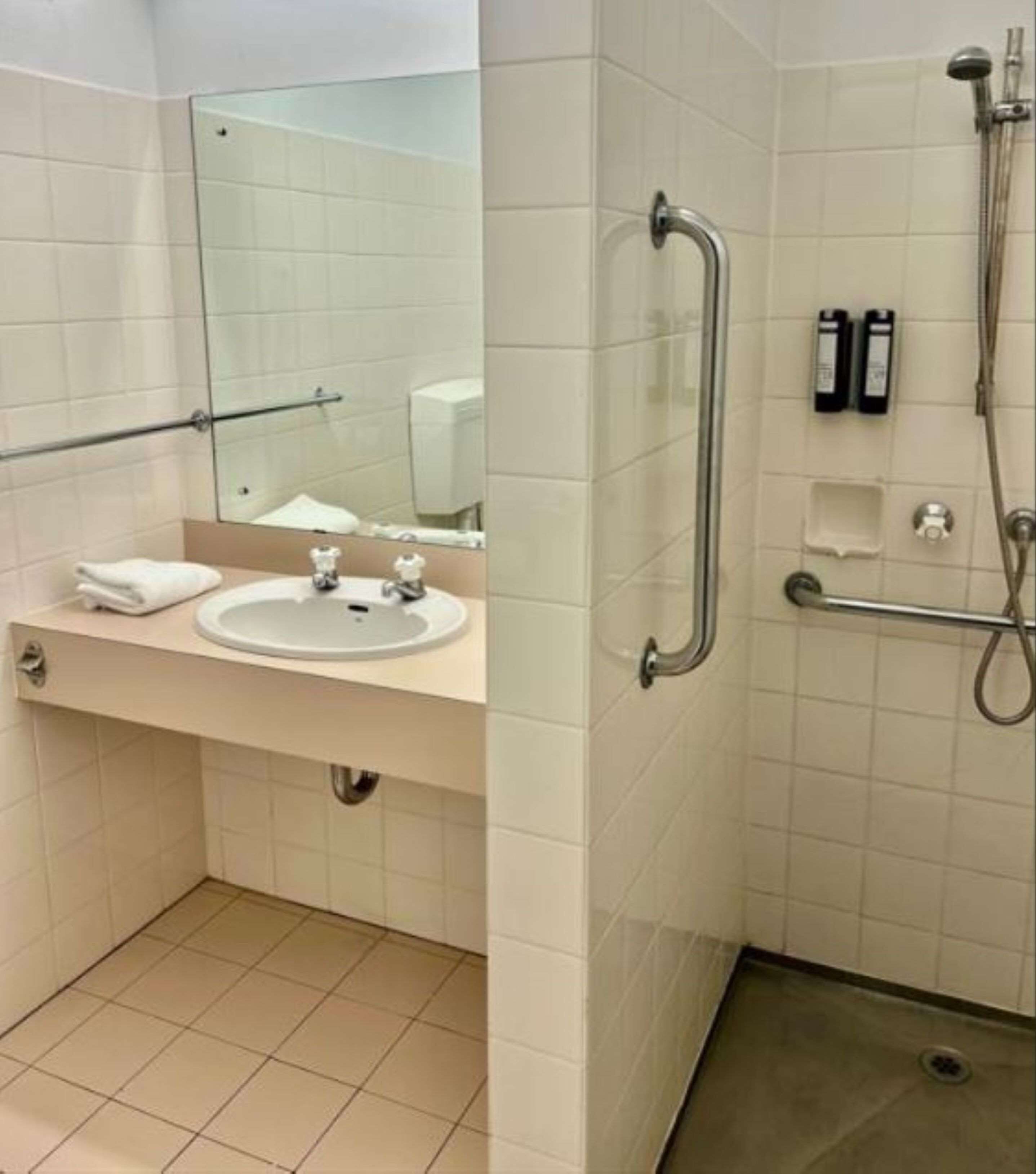 Un baño con lavabo, espejo y zona de ducha con barras de apoyo.