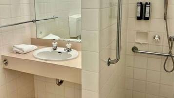A bathroom with a sink, mirror, and a shower area with grab bars.