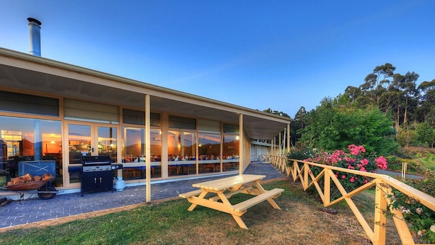 Un bâtiment moderne doté de grandes fenêtres, d’un espace extérieur aménagé pour s’asseoir et d’un coin barbecue.