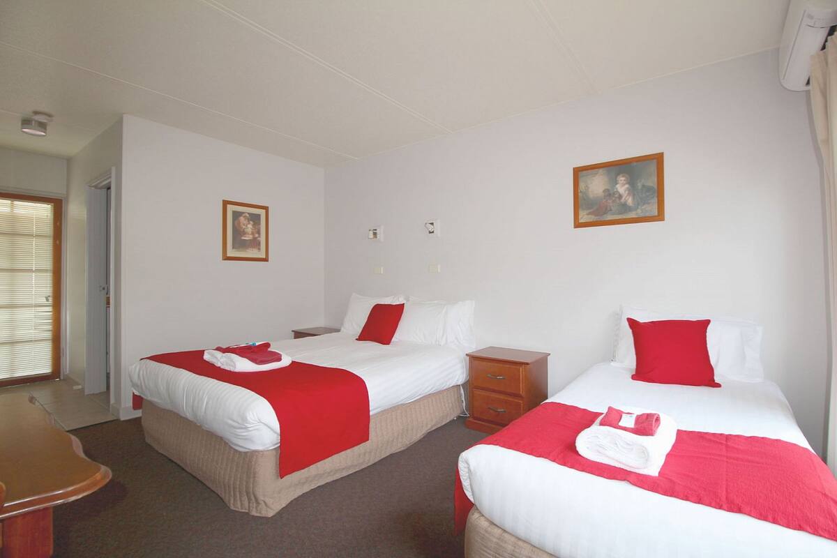 A hotel room with two beds, each with red and white bedding, a wooden nightstand, a small wooden dresser, and a painting on the wall.