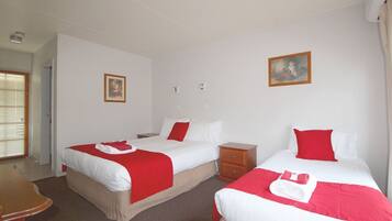 A hotel room with two beds, each with red and white bedding, a wooden nightstand, a small wooden dresser, and a painting on the wall.