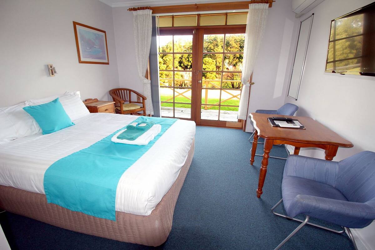 A hotel room with a bed, a desk, a chair, and a view of the outdoors.