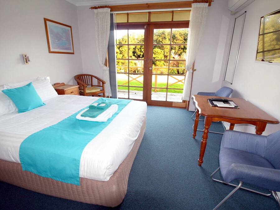 A hotel room with a bed, a desk, a chair, and a view of the outdoors.
