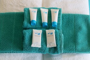 A green towel with five Crystal brand toiletries: two soaps, one shampoo, one conditioner, and one shower gel.