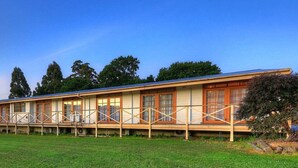 Une rangée de bâtiments d’un seul étage, dotés d’un toit plat, qui semblent être un hôtel ou un motel, avec un champ verdoyant au premier plan et des arbres en arrière-plan.