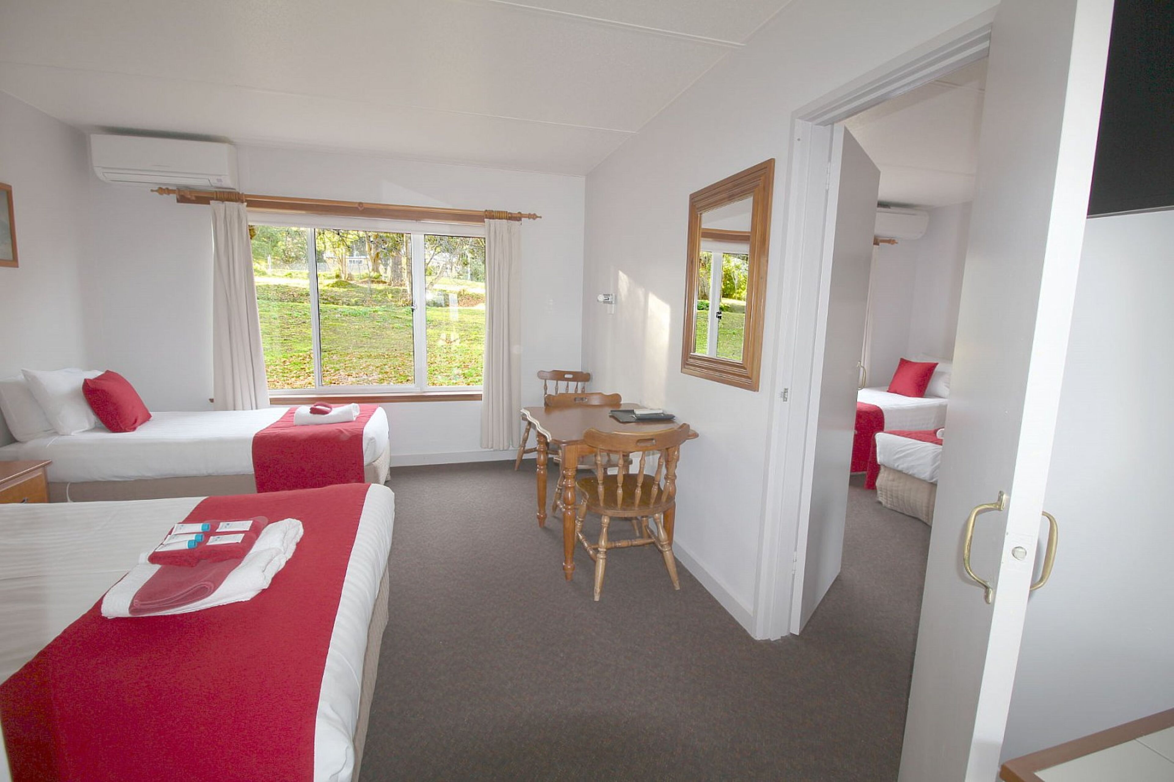 A hotel room with two beds, a dining table, and a view of the garden.