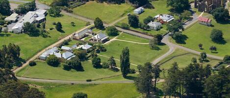 An aerial view of a rural area with several buildings, including a large circular structure with a dome roof, surrounded by green fields and a few scattered houses.