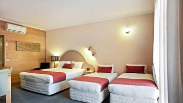 Quarto de hotel com três camas, uma escrivaninha e ar condicionado fixado na parede.