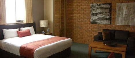 A hotel room with a bed, a coffee table, a sofa, and a brick wall.