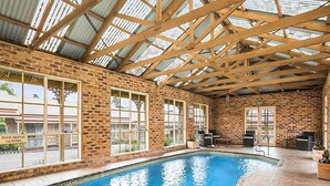 An indoor swimming pool with a brick wall, wooden beams, and large windows. - Quality Inn Colonial (Golden Square)