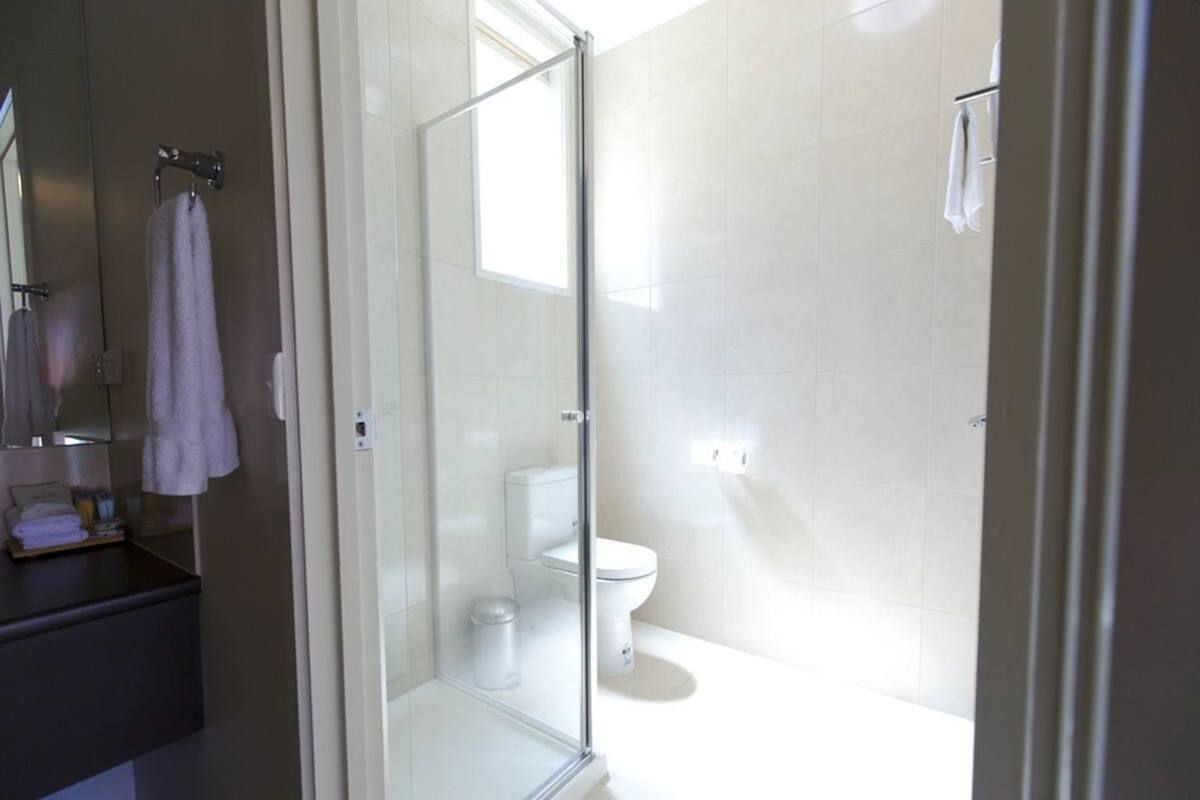 A bathroom with a glass shower enclosure, a toilet, and a sink with a mirror.