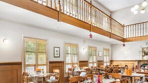 A dining area with wooden tables and chairs, large windows with blinds, and a wooden staircase. - Quality Inn Colonial (Golden Square)