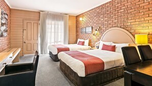 A hotel room with two beds, a desk, a chair, a lamp, and a brick wall. - Quality Inn Colonial (Golden Square)