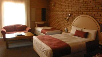 A hotel room with a brick wall, a large bed with two pillows, a smaller bed, a sofa, and a table.