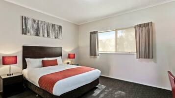 A hotel room with a bed, two bedside lamps, a window with curtains, and a wall-mounted artwork.