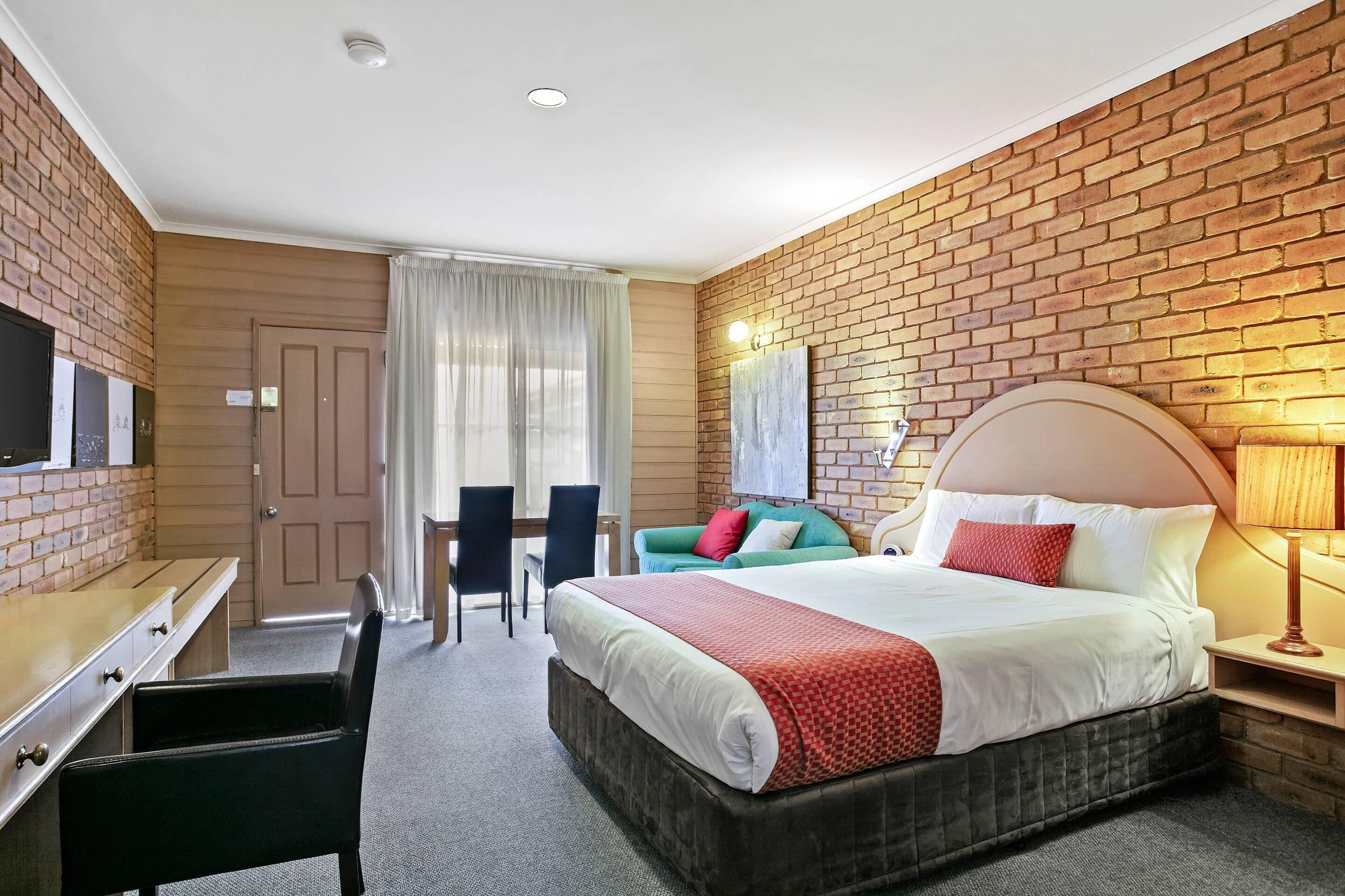 Una habitación de hotel con pared de ladrillo, cama con cabecera, escritorio y silla, y televisión.