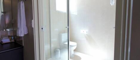 A bathroom with a glass-enclosed shower, a toilet, and a sink with a mirror.