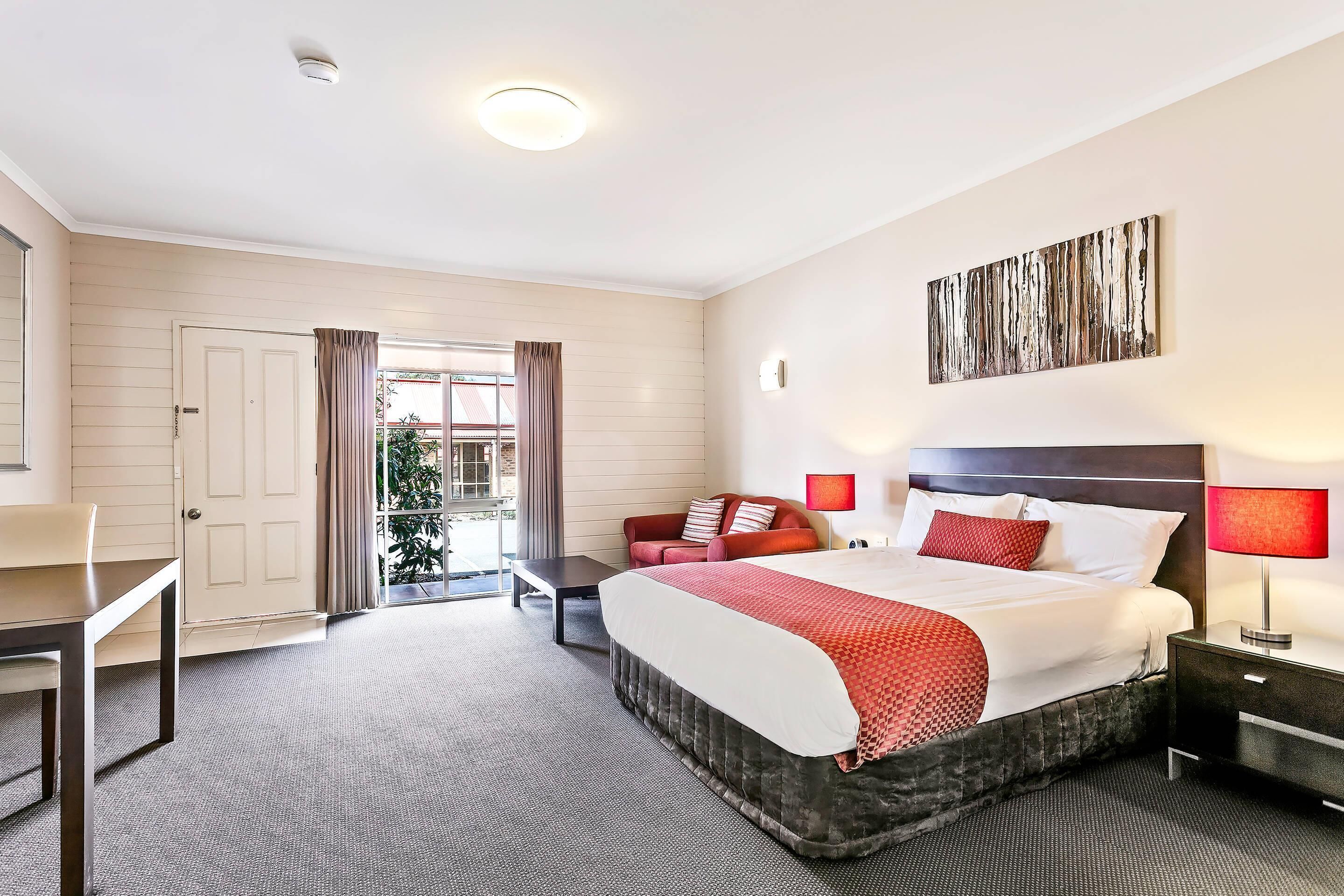 A hotel room with a large bed, a desk, a chair, a nightstand, and a window with curtains.