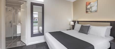Une chambre d’hôtel comprenant un lit, une table de chevet, une lampe, un tableau et un espace douche.