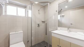 Un baño moderno con cabina de ducha de vidrio, inodoro y tocador con espejo.