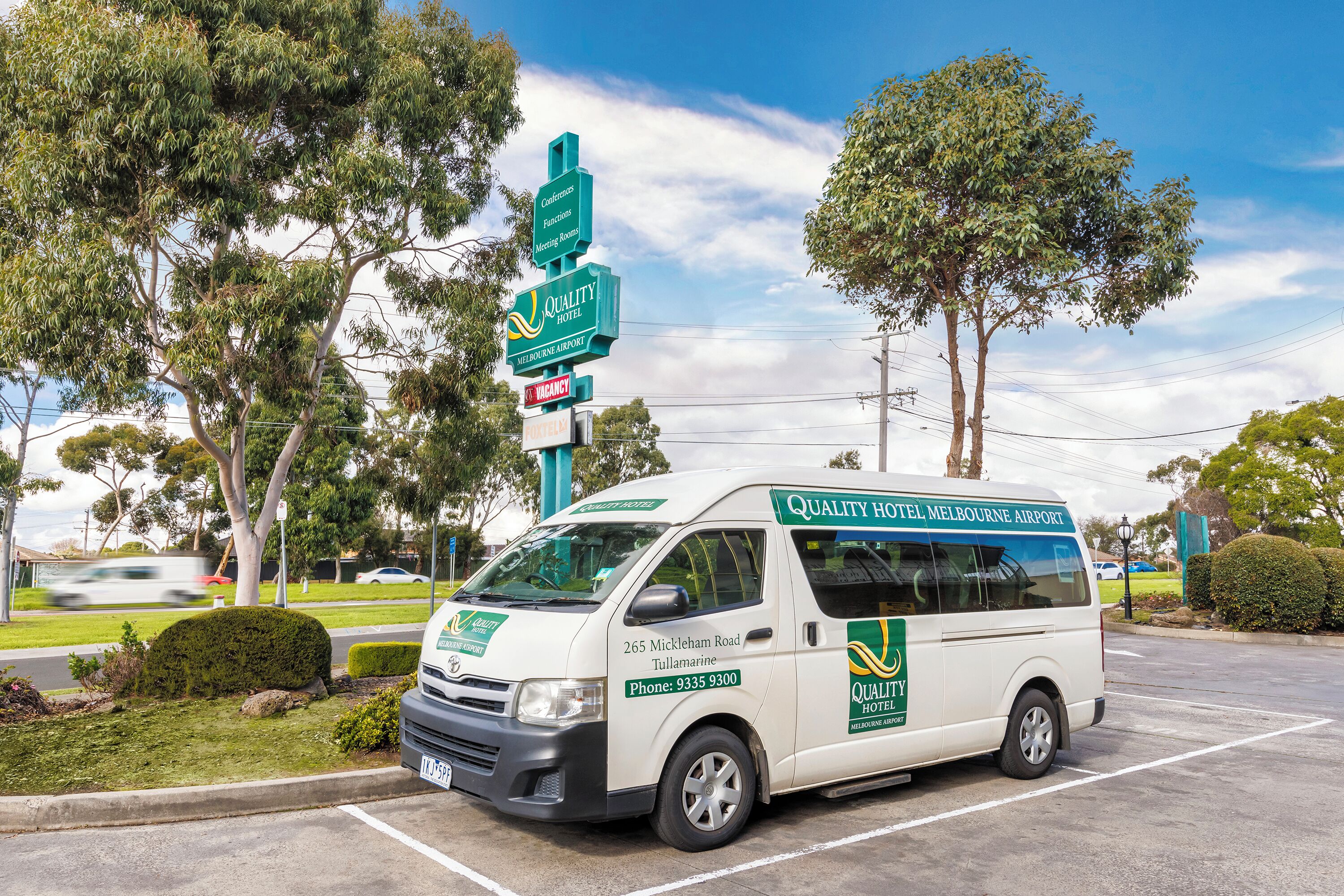 Una camioneta blanca estacionada en un estacionamiento con la marca 'Quality Hotel Melbourne Airport', indicando un servicio de hotel para viajeros.
