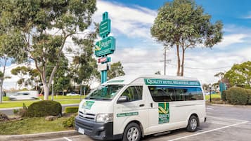 Una camioneta blanca estacionada en un estacionamiento con la marca 'Quality Hotel Melbourne Airport', indicando un servicio de hotel para viajeros.
