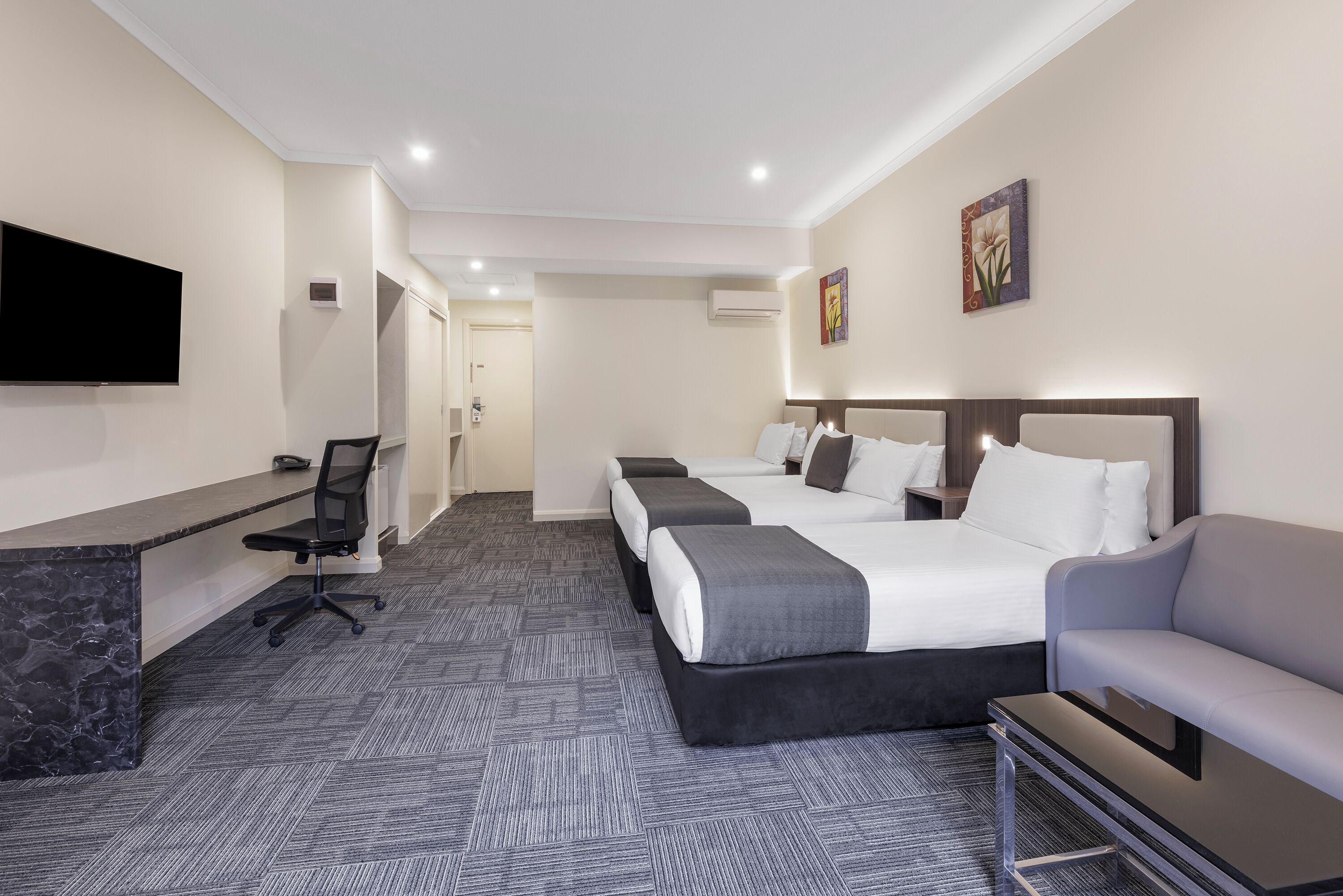 A hotel room with a desk, two beds, a TV, and a sofa.
