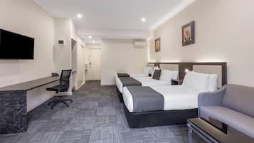 A hotel room with a desk, two beds, a TV, and a sofa.