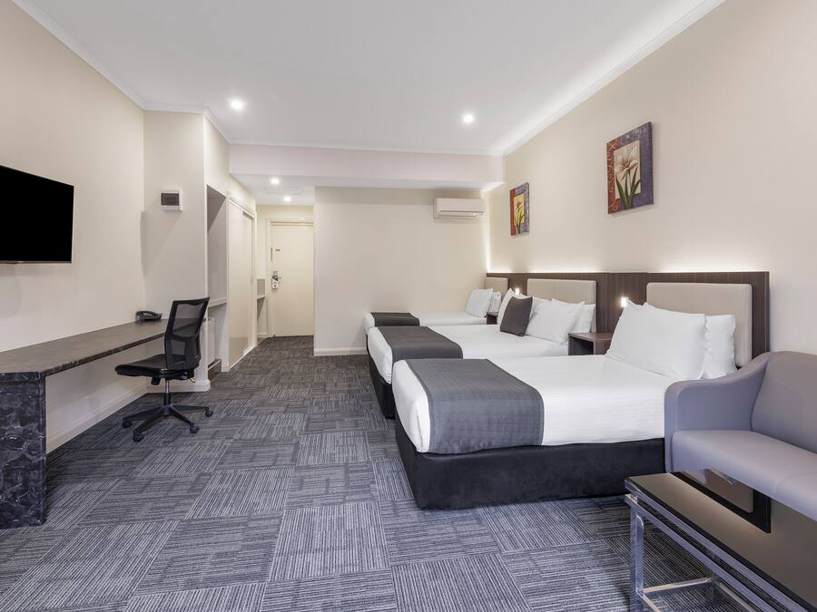 A hotel room with a desk, two beds, a TV, and a sofa.