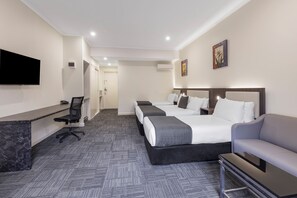 Ein Hotelzimmer mit Schreibtisch, zwei Betten, Fernseher und Sofa.