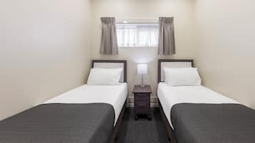 Habitación de hotel con dos camas individuales, una mesita de noche con lámpara y una ventana con cortinas.