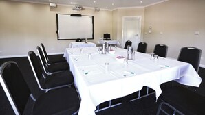 A conference room with a long table, black chairs, a projector screen, and a whiteboard. - Quality Hotel Melbourne Airport (Westmeadows)