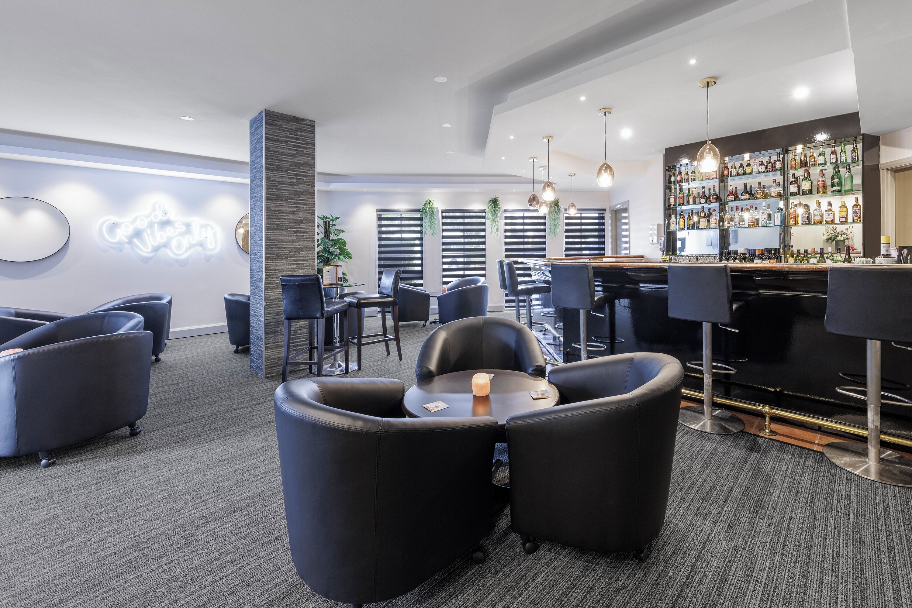 Un área de bar moderna con diversas opciones de asientos, incluyendo taburetes y sillones, y una amplia exhibición de licores.