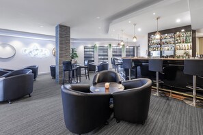 Un área de bar moderna con diversas opciones de asientos, incluyendo taburetes y sillones, y una amplia exhibición de licores.