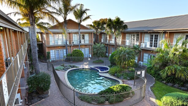 A courtyard with a swimming pool, surrounded by brick buildings and palm trees. - Quality Hotel Melbourne Airport (Westmeadows)