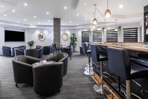 Un espace lounge moderne comprenant des sièges, un bar et un téléviseur à écran plat.