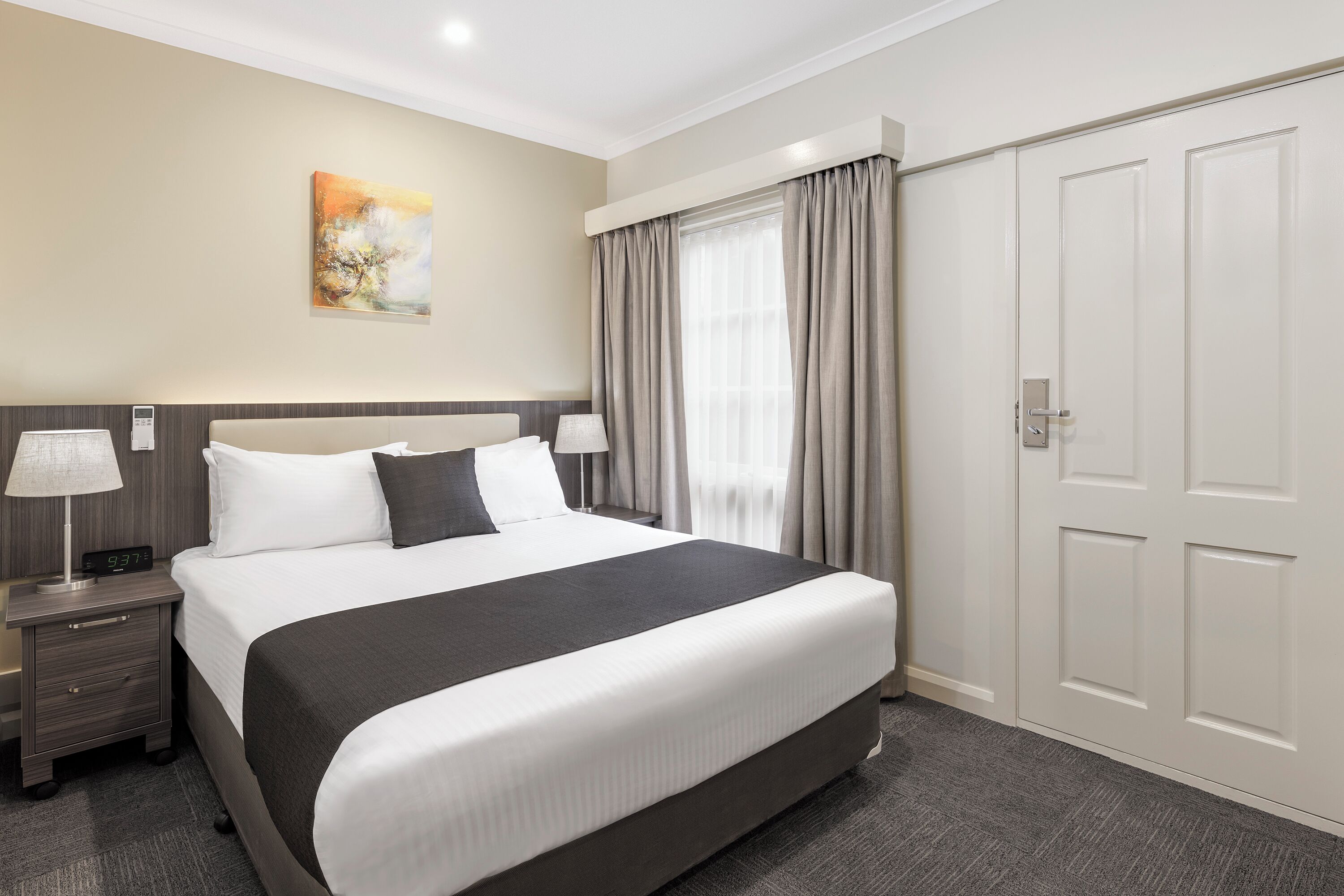 Une chambre d’hôtel avec un grand lit, une table de chevet avec une lampe, un tableau au mur et une armoire.