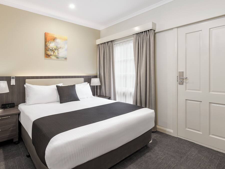 Una camera d'albergo con un letto grande, un comodino con una lampada, un quadro appeso e un armadio.