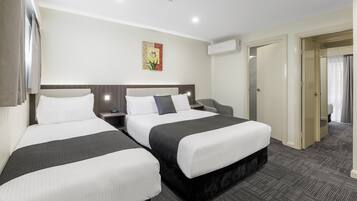 A hotel room with two beds, a nightstand, a wall-mounted air conditioner, and a door leading to another room.