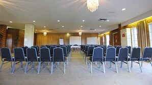 A conference room with rows of chairs, a projector screen, and a chandelier. - Quality Hotel Melbourne Airport (Westmeadows)