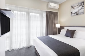 Ein Hotelzimmer mit einem Bett, Vorhängen, einer Wand-Klimaanlage, einem Gemälde und einer Nachttischlampe.