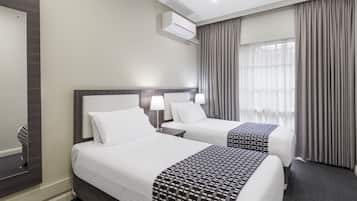 A hotel room with two beds, a nightstand, a lamp, an air conditioning unit, and a window with curtains.