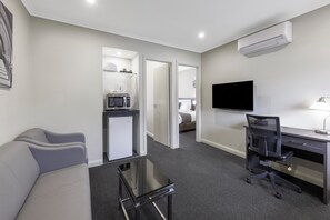 Habitación de hotel compacta con kitchenette, un televisor de pantalla plana, un escritorio con silla y un sofá.