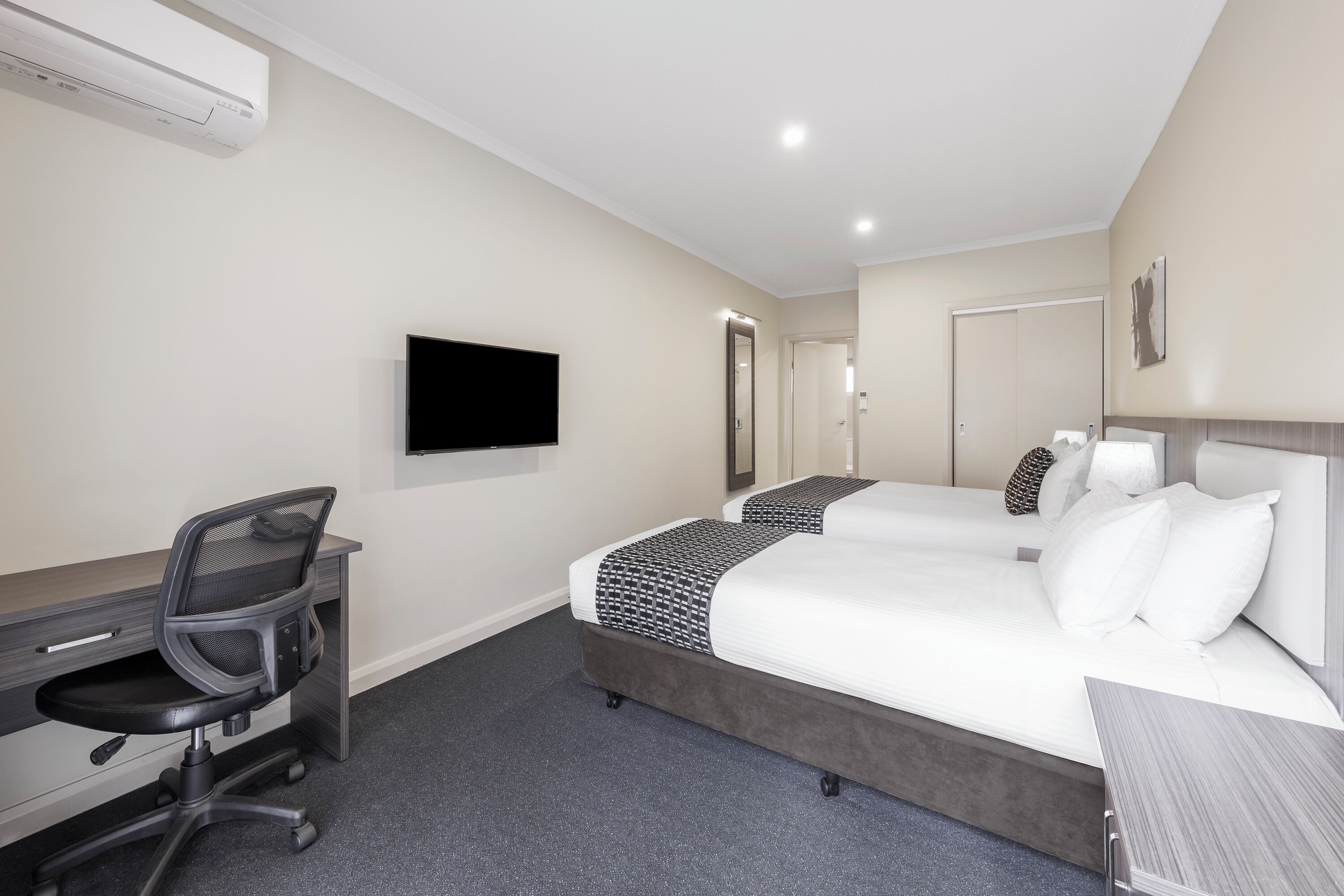 Habitación de hotel con cama, escritorio, silla, televisor de pantalla plana y espejo.